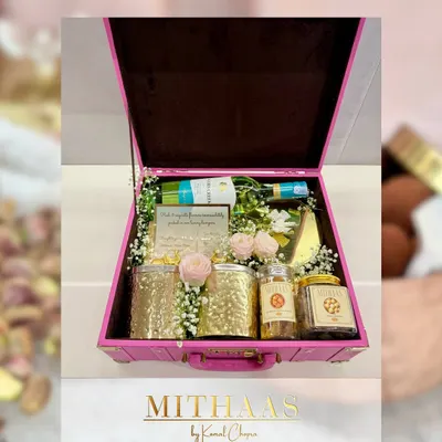 This custom hamper, built in a beautiful pink trunk, shows the variety you can choose from. It includes a bottle of non-alcoholic wine, jars of gourmet nuts, and a personalized note, all adorned with fresh roses.