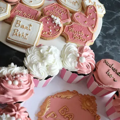 A complete 'Baat Pakki' dessert table setup. This includes custom cookies with blessings like 'Khush Raho', cupcakes, and a central plaque to mark the occasion.