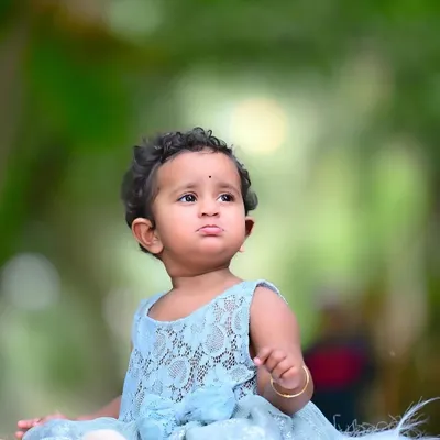 A beautiful outdoor portrait of a baby girl, lost in thought. The soft, natural background and her sweet expression make this a simple yet captivating image.