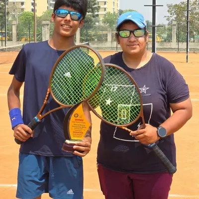 A milestone moment for Ayush Chaudhary, winning his first AITA National U-14 singles title. Here he is with his coach, holding their rackets and the winner's trophy on the clay court.