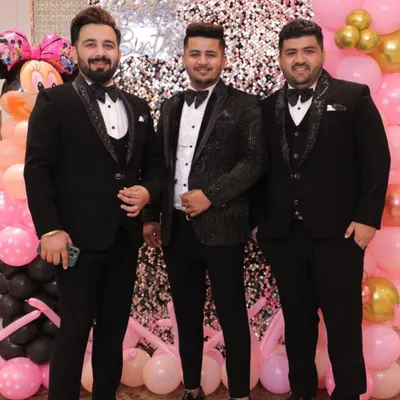 A trio of groomsmen in coordinated black tuxedos. While the base is classic, each tuxedo jacket has a unique texture and lapel design, showcasing individuality within a formal theme.