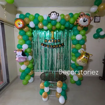 A classic jungle theme birthday decoration for a home setting. This setup includes a green and gold balloon arch, a shimmer curtain backdrop, and cute animal head foil balloons like a lion, tiger, and monkey.