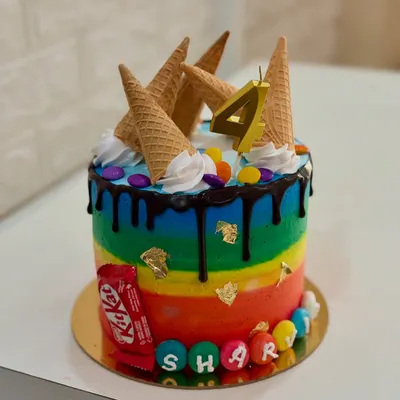 A vibrant rainbow cake that's perfect for any kid's birthday party. This one is topped with ice cream cones, a chocolate drip, and colorful candies for a fun, over-the-top look.