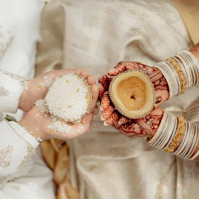 A close-up of a South Indian wedding ritual. This shot focuses on the hands of the couple, the intricate henna, and the symbolic offerings, capturing the beauty of the tradition.