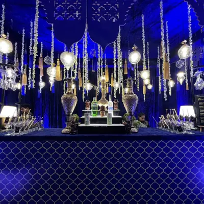 A wide view of our grand Sufi Night bar. The setup is defined by its rich royal blue fabric, intricate silver Moroccan patterns, and an elaborate overhead arrangement of hanging lights and tassels.