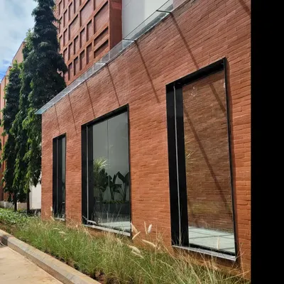The facade of the Campus Biovet office block, where an entire wall is clad in exposed brick. The glass roof of the protruding entryway reflects the sky, creating a beautiful contrast between the earthy brick and the open air.