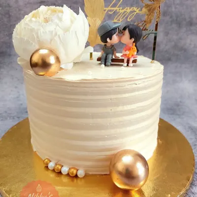This strawberry flavored cake is perfect for an anniversary or engagement. It features a clean, striped frosting finish, golden decorative spheres, and an adorable topper of a couple sharing a sweet moment.