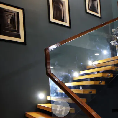 A detail of the floating wooden staircase. The glass railing with a wooden handrail provides safety without obstructing the view, and the framed architectural prints on the wall add to the sophisticated atmosphere.