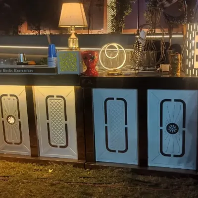 A stylish and modern bar counter rental for an outdoor event. This unit features backlit front panels and is decorated with contemporary lamps and accessories to create a chic service area.