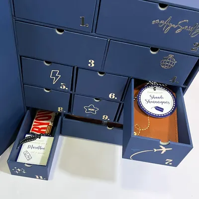A peek inside the groomsmen advent calendar. Each numbered drawer reveals a unique, personalized gift, like a custom passport holder or a chocolate bar for a mid-wedding marathon.