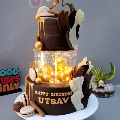 A breathtaking two-tier chocolate cake with a lit-up separator, gold drip, and artistic chocolate sails. This cake is pure modern elegance.