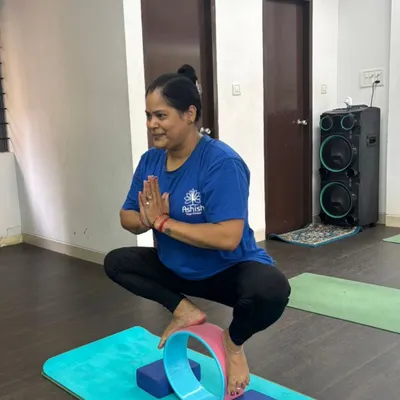A student uses a yoga wheel and blocks for support in Malasana (Garland Pose), helping to open the hips while maintaining balance.