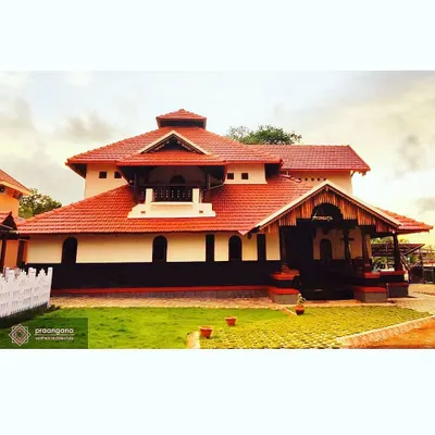 The exterior of the Udupi residence, showcasing its classic Kerala-inspired architectural style with a sloping tiled roof, crisp white lime-plastered walls, and a green lawn.