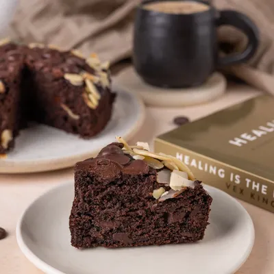 A perfect slice of chocolate almond cake paired with coffee, styled with a book to create a cozy, relaxing afternoon vibe.