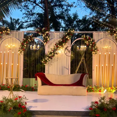 A beautifully lit stage for a wedding reception. The design features modern arches, floral arrangements in red and white, and elegant candelabras, creating a romantic focal point for the evening.