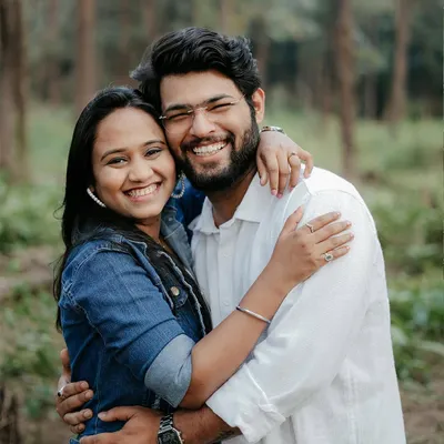 A bright, happy portrait of a couple hugging and smiling directly at the camera in a forest setting. This shot radiates pure joy and is perfect for capturing your fun-loving personalities.