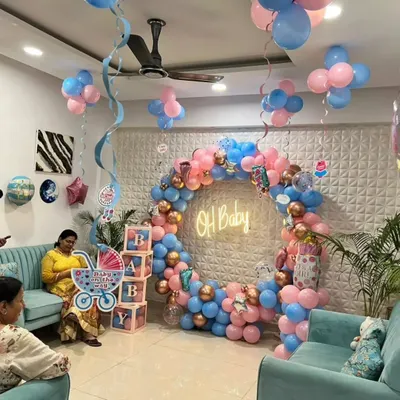 A full room setup for a baby shower. This includes a circular balloon arch with an 'Oh Baby' neon sign, 'BABY' display boxes, and balloon clusters on the ceiling.