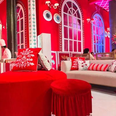 A comfortable and stylish seating lounge from the 'Laal Ishq' event. The vibrant red furniture, custom-embroidered cushions, and arched windows are all inspired by the iconic Villa Palladio in Jaipur.