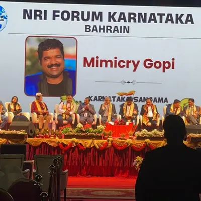 On stage at the Karnataka Sansama event organized by the NRI Forum Karnataka in Bahrain. My name and photo are displayed on the big screen.