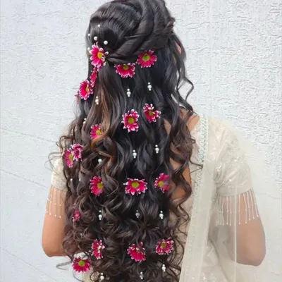 A stunning open hairstyle with cascading curls, decorated with bright pink flowers and pearls. This is a beautiful choice for a mehendi or sangeet ceremony.