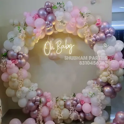 An elegant "Oh Baby" shower decoration featuring a circular balloon ring in pastel pink, white, and chrome, adorned with artificial flowers.