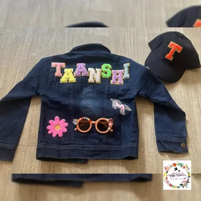 A custom denim jacket for a child named Taanshi. The back is decorated with her name in colorful patchwork letters, along with a unicorn and flower patch. The set also includes a matching initial cap.