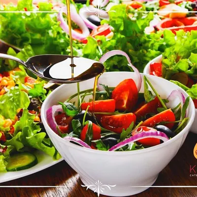 A fresh and vibrant salad featuring mixed greens, cherry tomatoes, and red onions, being dressed with extra virgin olive oil. We believe in using simple, high-quality ingredients to create delicious and healthy salad options.