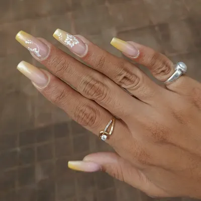 A beautiful set of long, square-shaped nails with a yellow ombre base and delicate, hand-painted white floral details.
