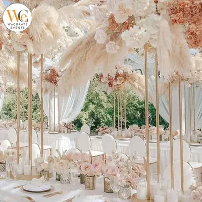 A breathtaking dining setup featuring tall centerpieces with pampas grass and white roses. This creates a sense of height and drama, perfect for a luxurious wedding reception.
