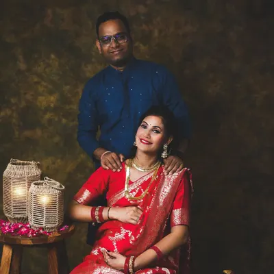 A beautiful traditional portrait of an expecting couple. The rich red Banarasi saree looks stunning against the classic painted backdrop.