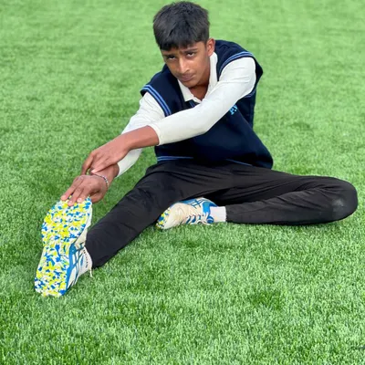 A young player performs a hamstring stretch on the lush astroturf. Flexibility is a key component of our fitness routine, helping with injury prevention and agility on the field.