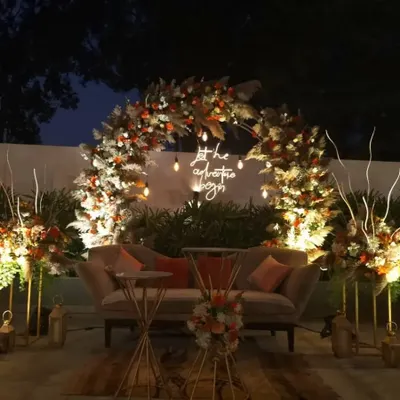 This breathtaking reception stage features a semi-circular arch of pampas grass and florals, with a neon sign that reads 'let the adventure begin'. The design is perfect for a modern, bohemian-themed celebration.