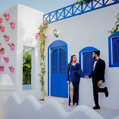 Yash and Priyanshi pose against a beautiful white building with vibrant blue doors, reminiscent of a Greek island. This set is perfect for couples wanting a clean, bright, and destination-style photoshoot.