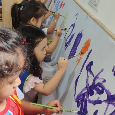 A group of young artists completely absorbed in creating a large-scale abstract mural. This collaborative painting activity encourages teamwork, communication, and shared creative expression.