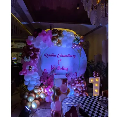 A magical butterfly-themed first birthday for Radha. The round backdrop is surrounded by a pink and rose gold balloon arch, with a large light-up number '1' to mark the special milestone.