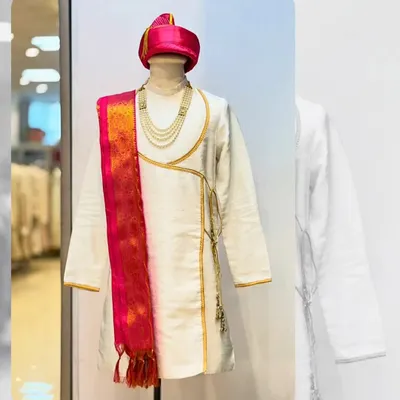 This is a classic Peshwai look, featuring a white angarkha-style kurta with a vibrant pink and gold dupatta. The pearl necklace completes the royal ensemble.