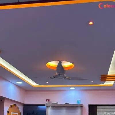 This living room ceiling demonstrates a combination of lighting techniques. Warm cove lighting provides a soft, ambient glow around the central fixture, while cool-toned recessed spotlights ensure the space is well-lit and functional.