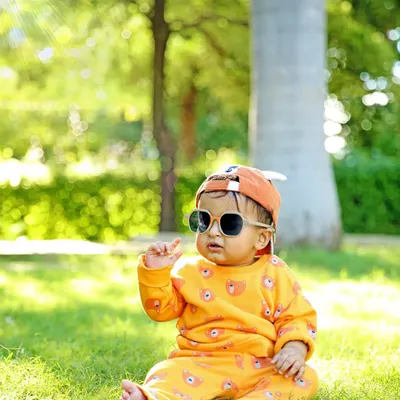 A cool and casual pose from a baby photoshoot in a park. The natural sunlight and green background create a beautiful, soft bokeh effect, making the little one the star of the show.