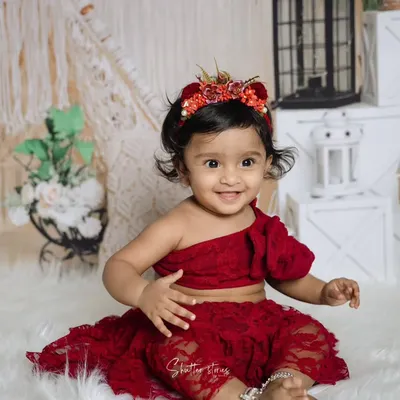 A perfect first birthday portrait! This little girl is all smiles in her red lace outfit, sitting on a fluffy white rug with a bohemian-style backdrop.