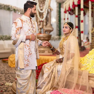 For this South Indian wedding, I designed the groom's off-white and gold embroidered sherwani and dhoti to perfectly complement the bride's traditional gold Kanjivaram saree, creating a timeless and regal look for their special day.