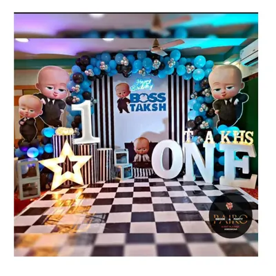 A complete Boss Baby theme for Taksh's first birthday. The setup includes a custom-designed stage with a striped backdrop, checkered flooring, light-up marquee letters, and multiple character cutouts for a fun, immersive photo zone.