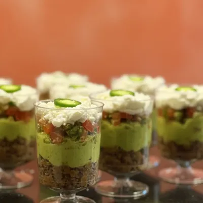 My Mexican Layered Cups are a flavor bomb. I layer savory beans, fresh guacamole, zesty salsa, and cool sour cream, topped with a slice of jalapeño for a little kick. They are a party in a cup.