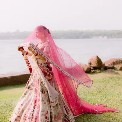A stunning bridal portrait by the sea in Goa. The bride's pink veil flowing in the wind against the water creates a breathtaking, ethereal image that is both grand and graceful.