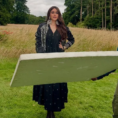 A behind-the-scenes moment on location in Scotland. Mrunal wears a custom-designed black dress and an embroidered jacket, a look that perfectly captures Rabia's blend of traditional motifs and modern silhouettes. The dramatic earrings and boots complete this signature character style.