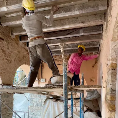 Two craftsmen work on restoring the timber ceiling beams of a historic school. This delicate process involves strengthening the original structure while preserving its aged character, a core principle of our conservation work.