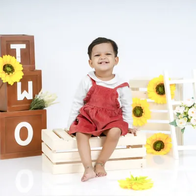 Celebrating the "Terrific Twos"! This little girl's bright smile is the centerpiece of her second birthday photoshoot, complete with "TWO" blocks and sunflowers.