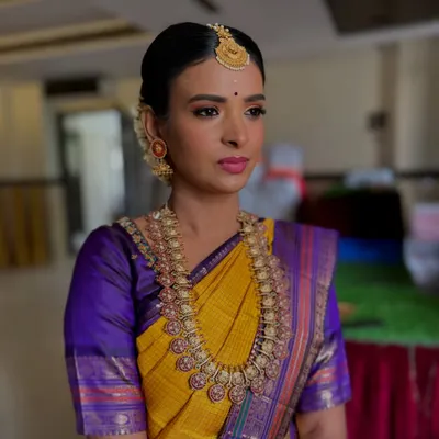 A classic South Indian bridal portrait. The makeup is designed to enhance her sharp features, with a focus on the eyes and a bold lip that matches the temple jewelry and silk saree.
