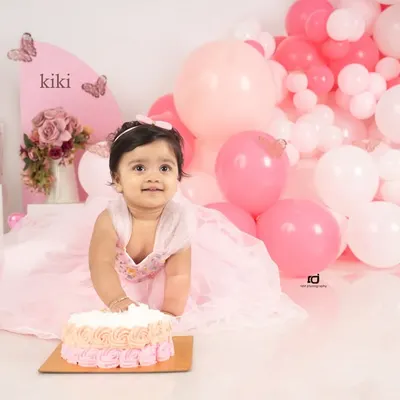 The moment of anticipation right before the cake smash begins. This little girl in her pink dress, with a butterfly-themed setup, is all smiles for her first birthday.