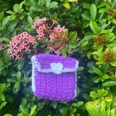 My handmade crochet pouch in purple and white, sitting in a bush. It's perfect for keeping your AirPods, coins, or other small treasures safe.