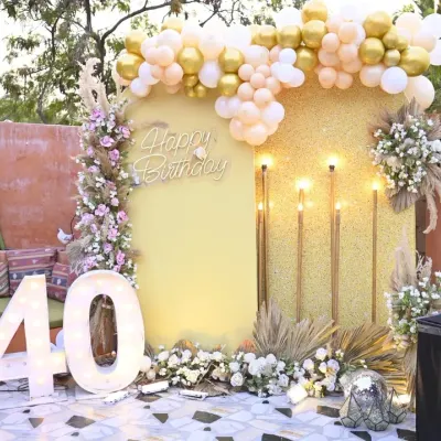 A fabulous 40th birthday celebration with a gold and glitter theme. The setup includes a shimmering backdrop, a large light-up '40', and boho-chic floral arrangements with pampas grass.